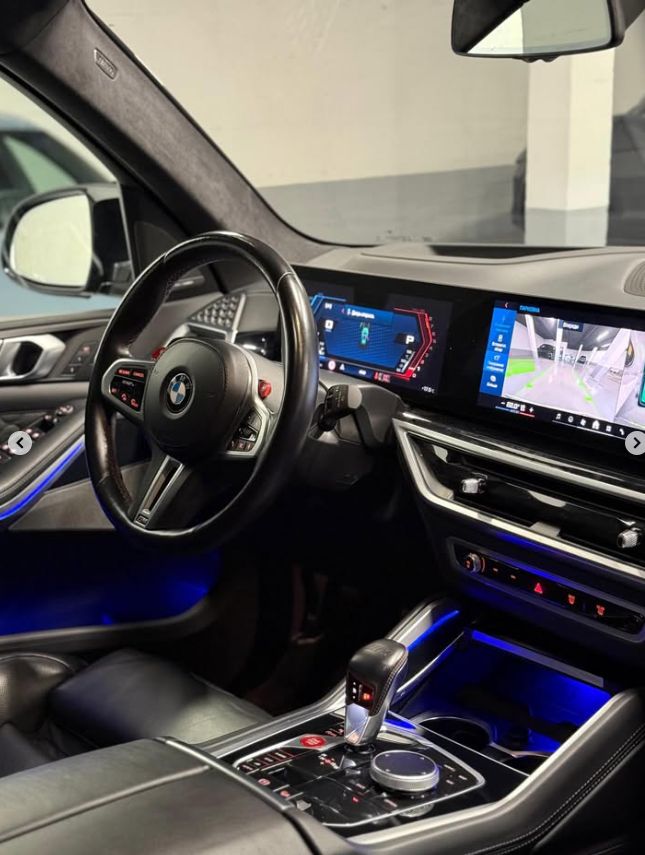 Interior view of a modern BMW with a digital cockpit, leather steering wheel, and ambient blue lighting.
