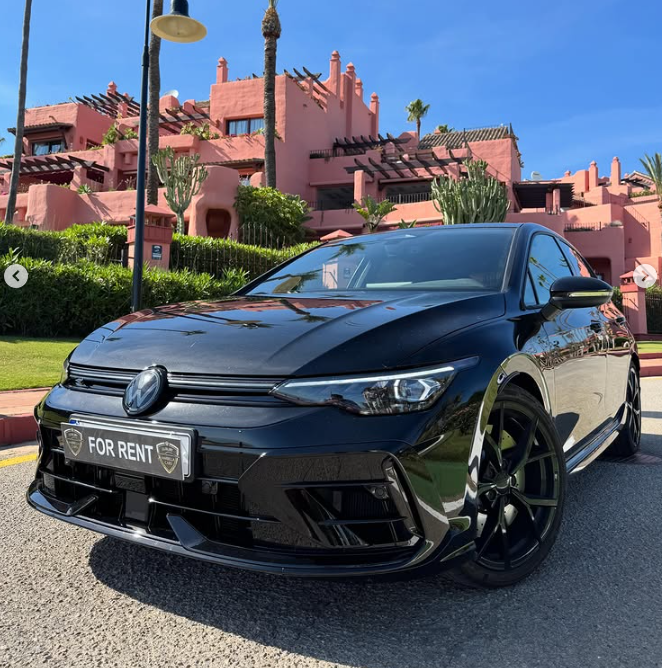 Black Volkswagen Golf rental car parked in front of a luxury pink resort with palm trees.