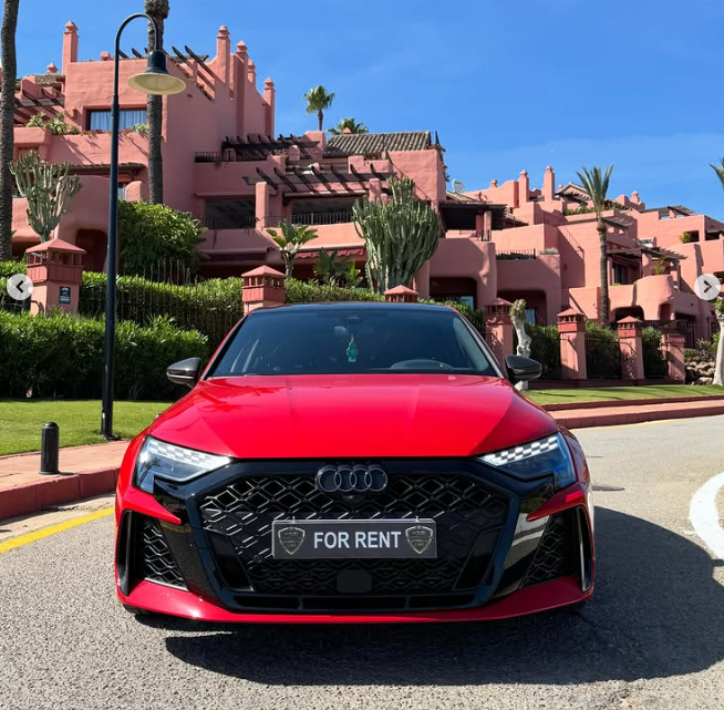 Red Audi RS3 luxury car rental parked in front of a pink Mediterranean resort building.