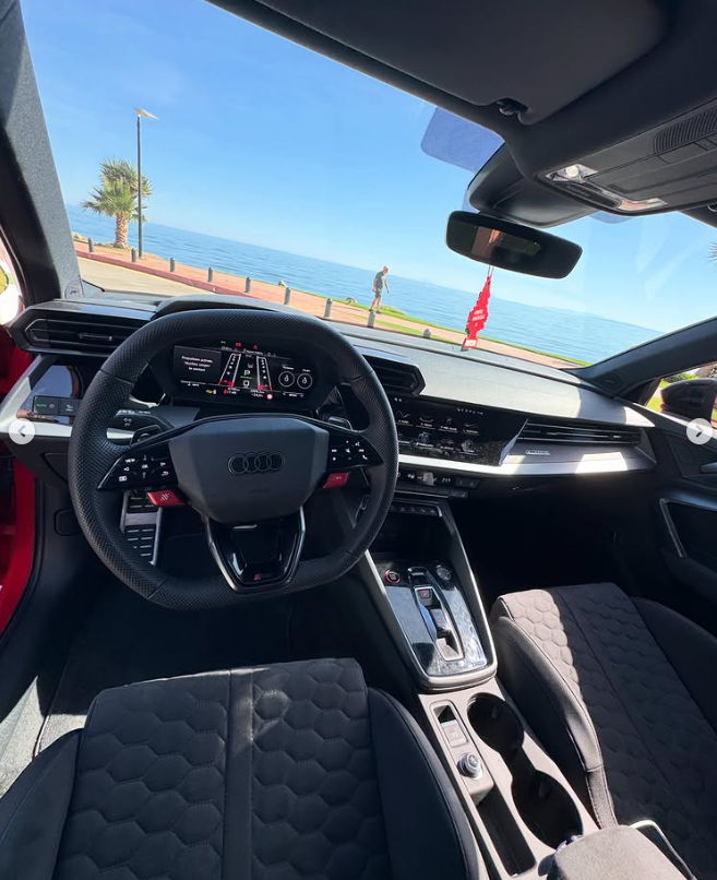 Modern Audi RS3 interior with a digital cockpit and leather steering wheel parked by the ocean.