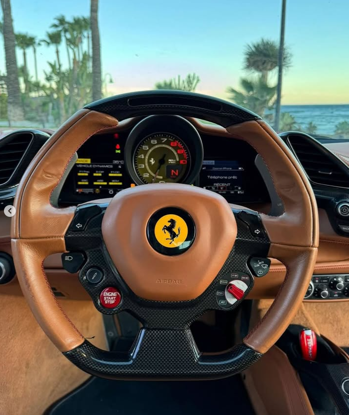 Luxury Ferrari interior featuring a tan leather and carbon fiber steering wheel with the prancing horse logo.