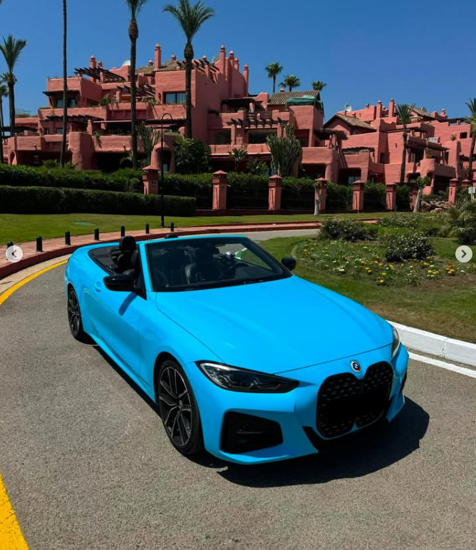 A bright blue convertible BMW parked on a sunny driveway in front of a pink Mediterranean style luxury resort.