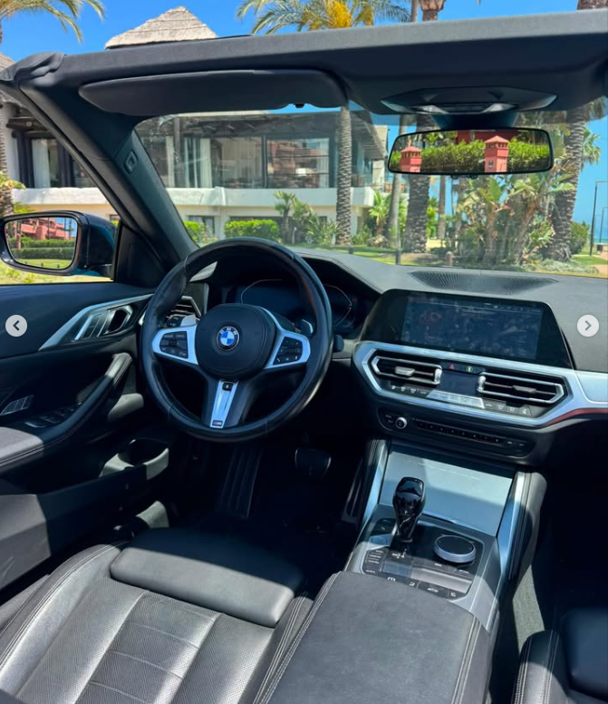 Interior view of a modern BMW convertible luxury car dashboard and steering wheel parked in a sunny tropical location.