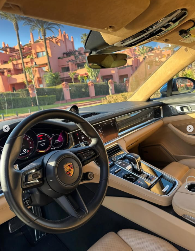 Luxury Porsche interior with tan leather seats and a digital dashboard parked near a coastal resort.