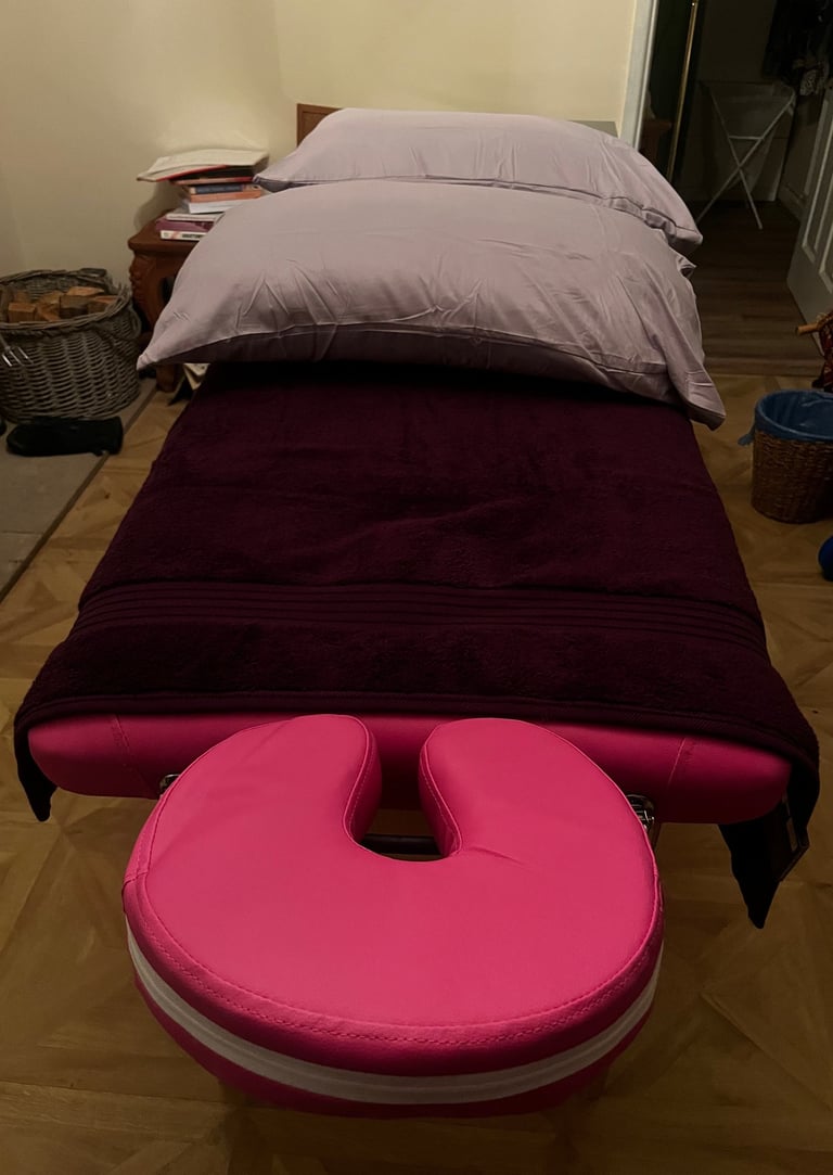 Image shows a pink massage table with dark purple towel covering it and lilac pillows