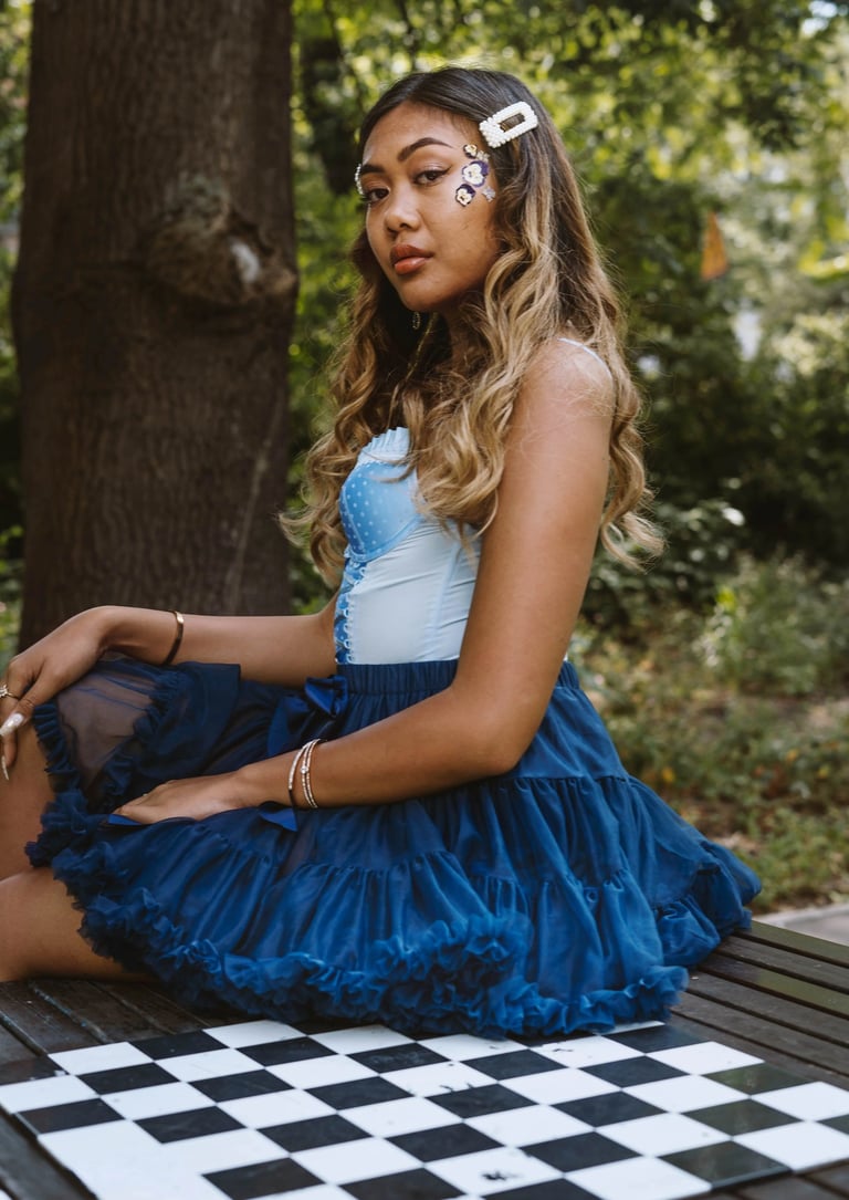 Portrait photo of a young Indonesian woman in a park with a chess table and whimsical blue dress