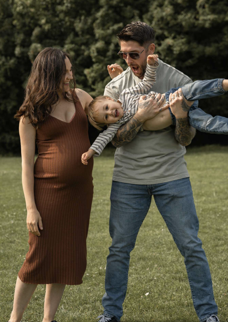 Pregnant woman laughing father is lifting his son