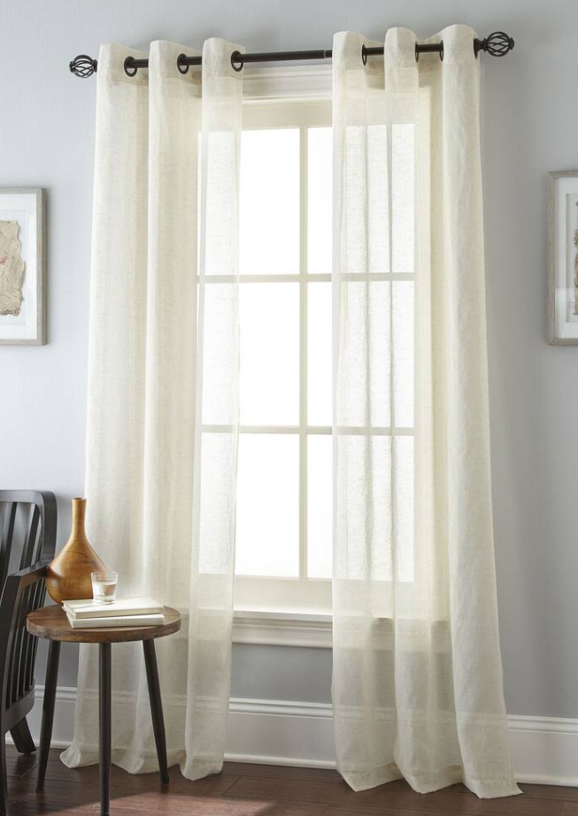 Elegant cream linen sheer curtains hanging on a dark rod over a bright window in a modern room.