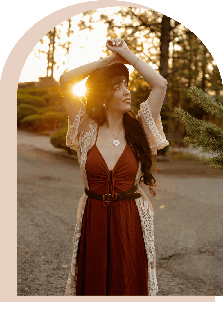 Ryanne in boho style outfit and hat posing at sunset in a scenic outdoor park setting.