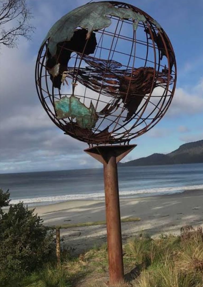 Verdigris metal globe sculpture on the beach with a mother whale and her calf in the middle of it