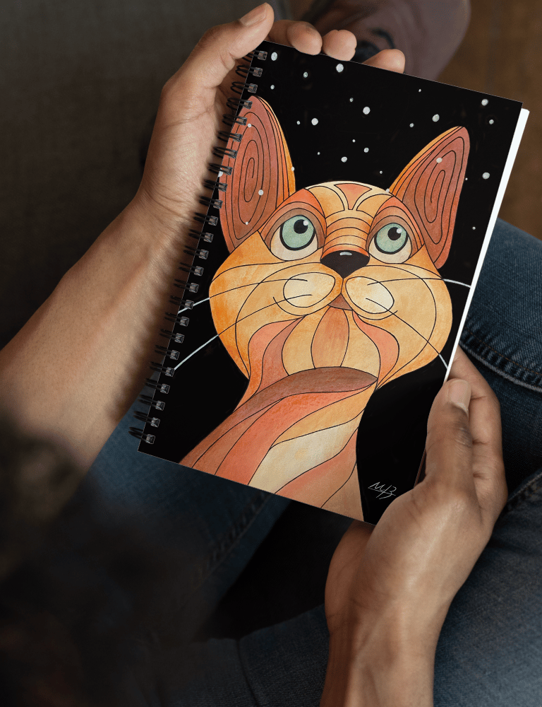 Person holding a spiral notebook featuring a whimsical cat art illustration by Mara Branco.