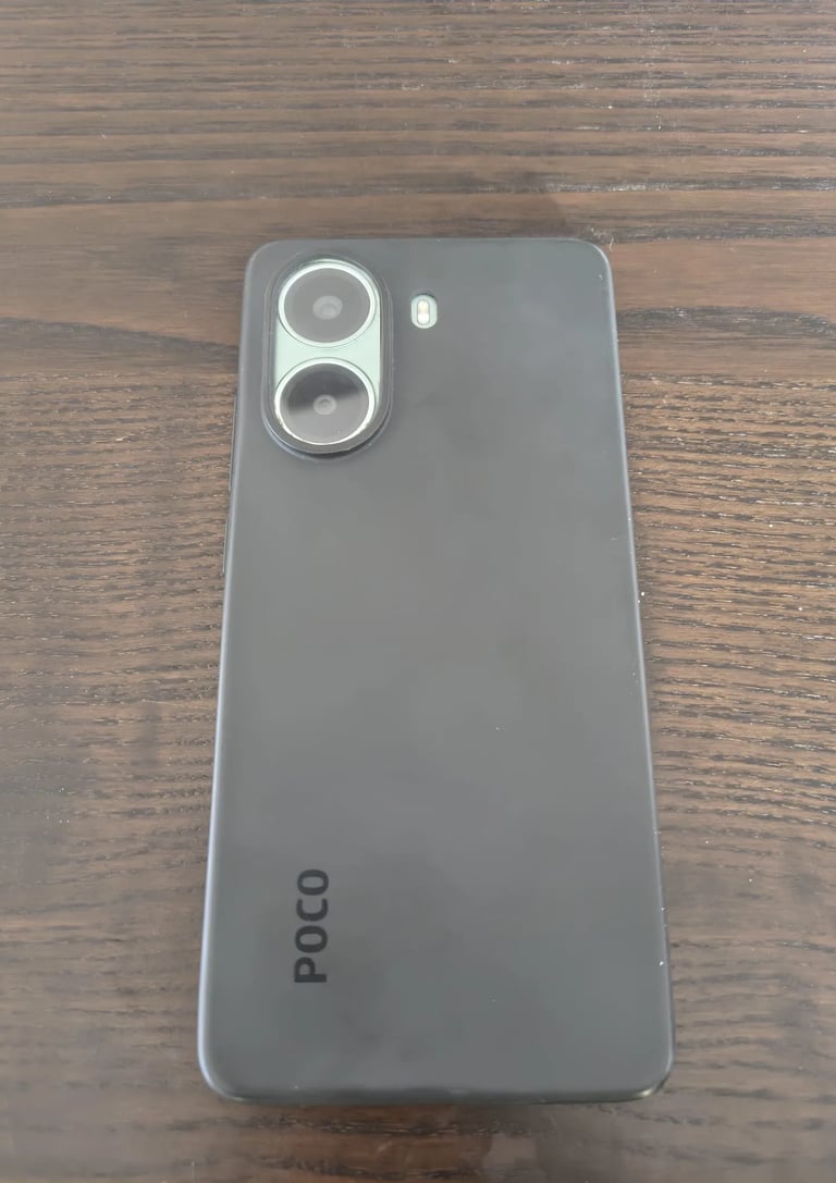 Review do telemóvel Poco mostrando o painel traseiro cinzento com lentes fotográficas sobre a mesa.