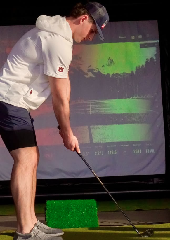 A male golfer practicing his swing on an indoor golf simulator with performance data tracking.