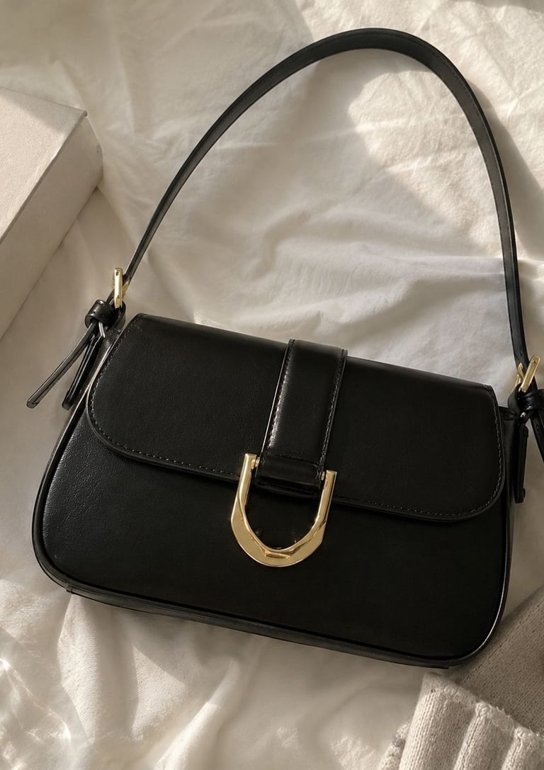 Woman wearing a black leather shoulder bag with gold buckle.