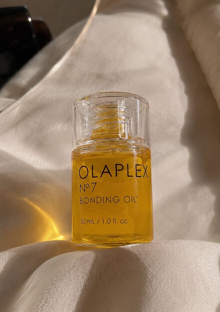 Close-up aesthetic photo of Olaplex No.7 Bonding Oil on soft beige satin fabric.