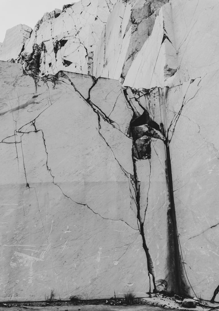Black and white texture of a cracked white marble quarry wall with jagged stone surfaces.