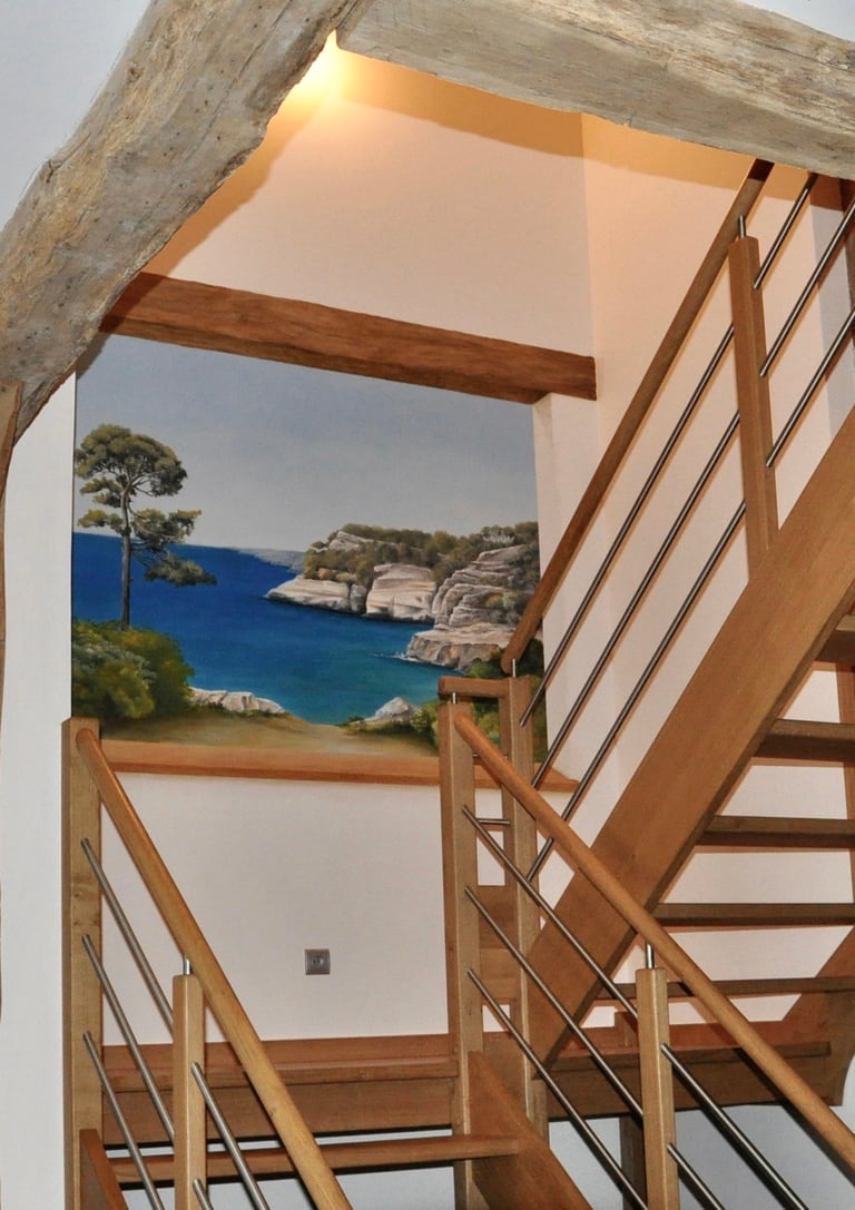 Une ouverture en trompe-l'oeil dans une cage d'escalier, invite au voyage en bord de mer. Le faux bois intègre l'ensemble.
