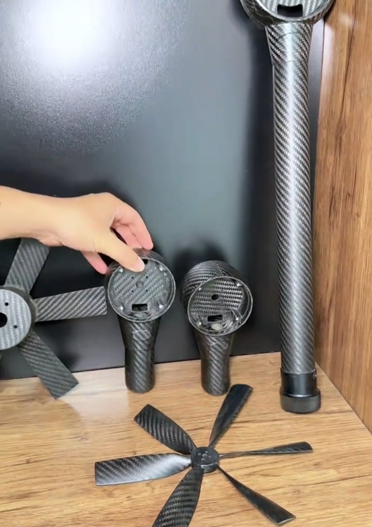 Custom lightweight carbon fiber drone parts including propeller blades and motor mounts on a wooden shelf.