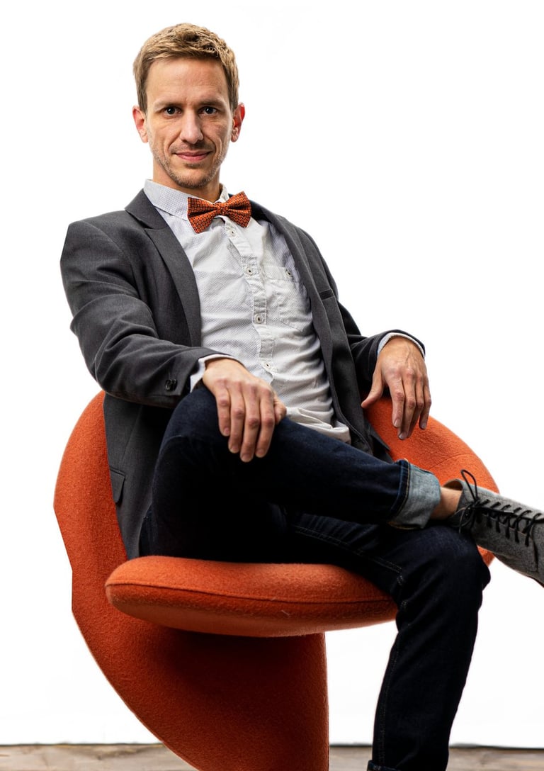 Remy sits in a chair wearing a sportcoat and bowtie