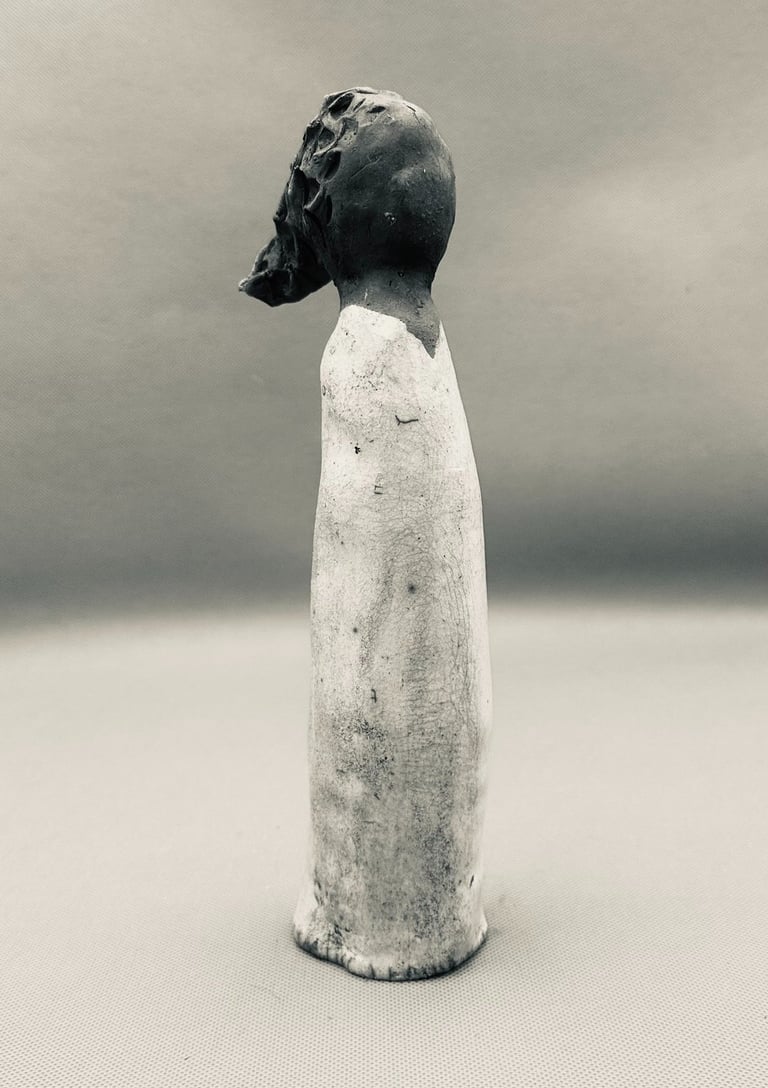 A handmade ceramic figurine of a slender woman in a long white dress, artfully crafted with dark clay details