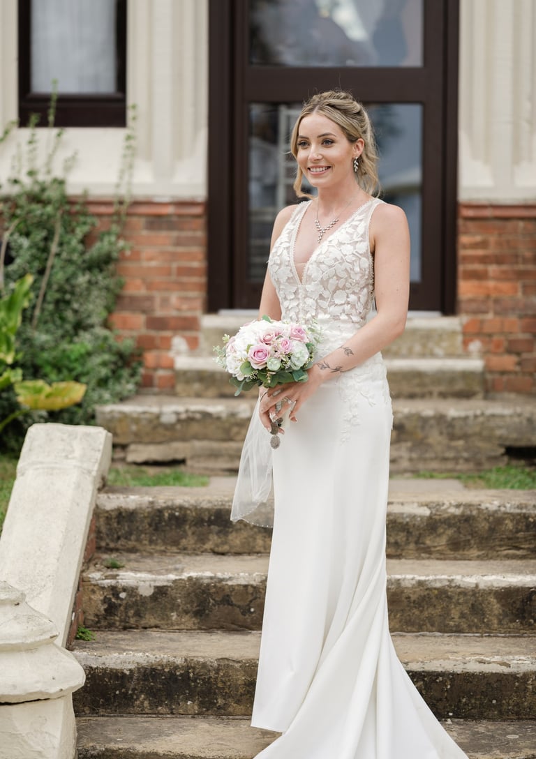 Bride snading in front of highley manor holding a bouquet 