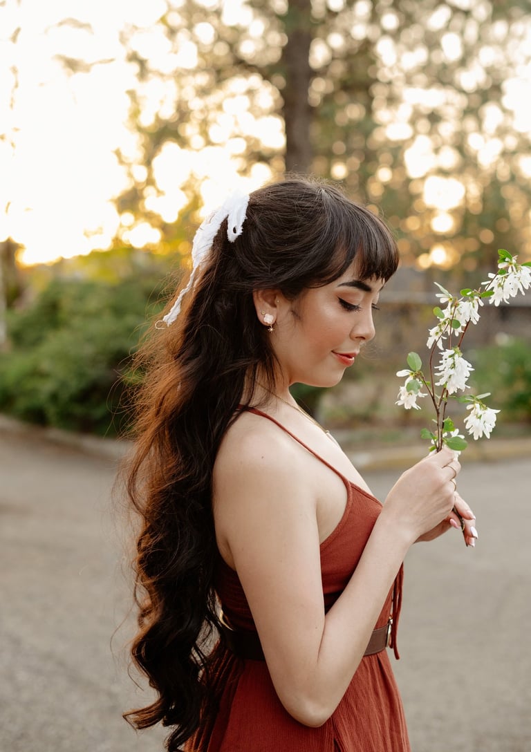Side profile of Ryanne with long hair and a hairbow holding branch of blossoms in golden hour light.