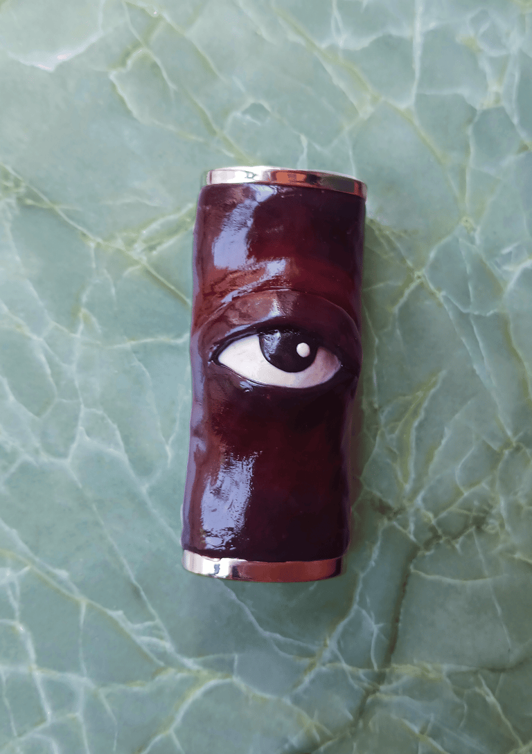 Shiny maroon hand-made lighter case with a sculpted 3D eye in the middle. 