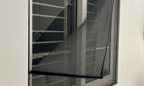 Close-up of a freshly installed mosquito net on a balcony window in Bangalore, sunlight filtering th