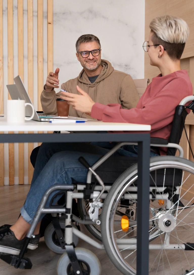 NDIS participant in a wheelchair having a discussion with a support worker at a desk