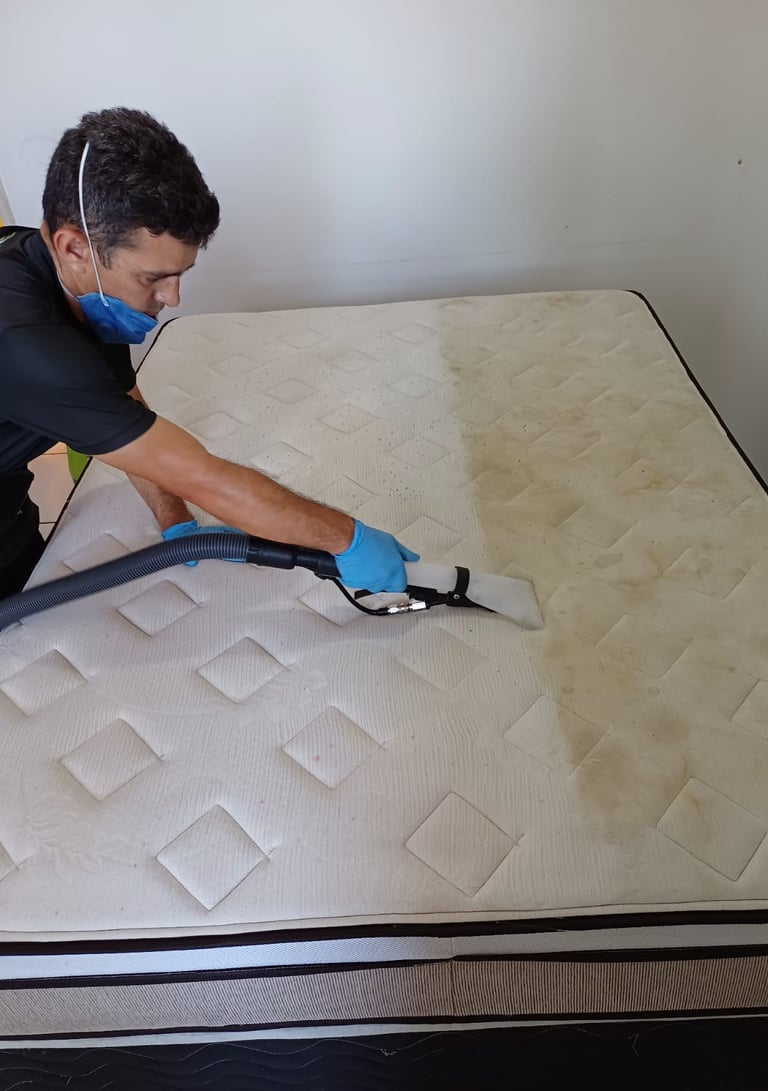 a man in a black shirt and blue gloves cleaning a mattress