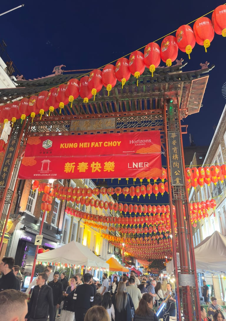 Crowded London Chinatown gate decorated with red lanterns and banners for Chinese New Year celebrations.