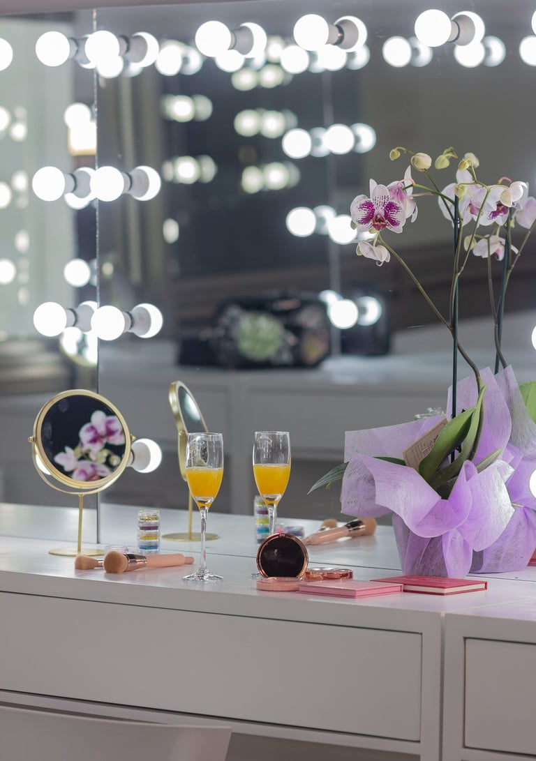 Tocador de lujo con espejo Hollywood iluminado, mimosas, pinceles de maquillaje y orquídea violeta.