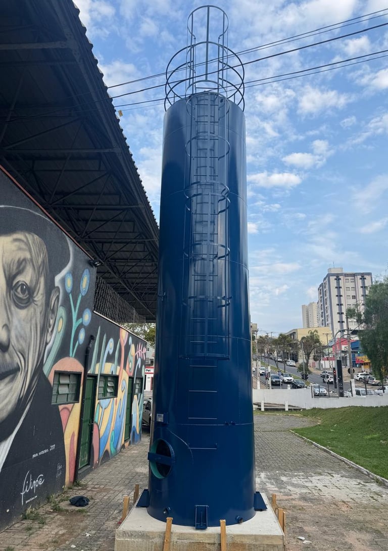 Reservatório metálico urbano com grafite e paisagem de cidade ao fundo"