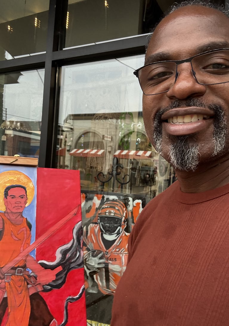 A smiling artist stands next to his vibrant canvas paintings in progress.