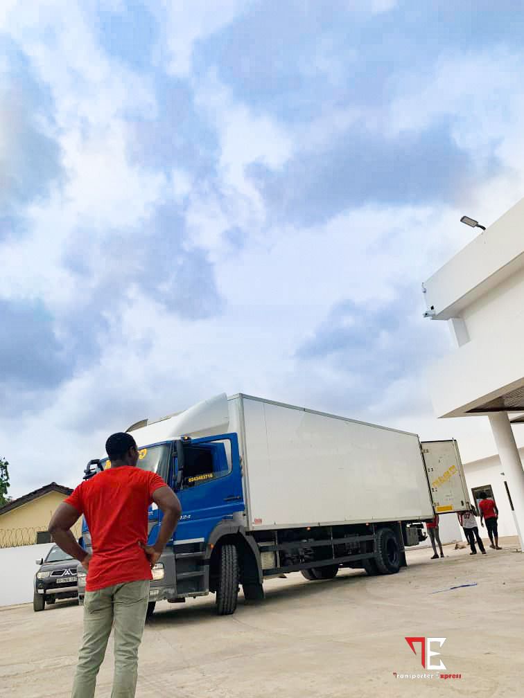 A confident man in a red t-shirt and khaki pants stands with hands on hips, overseeing operations be