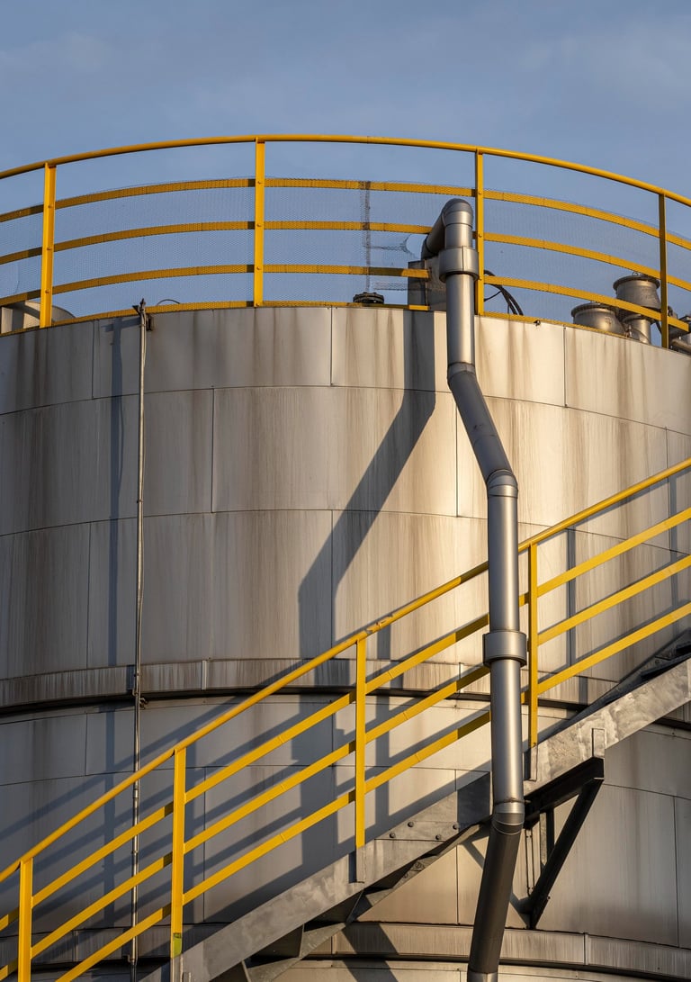 Tanque industrial de almacenamiento plateado con barandales de seguridad amarillos y escaleras metál