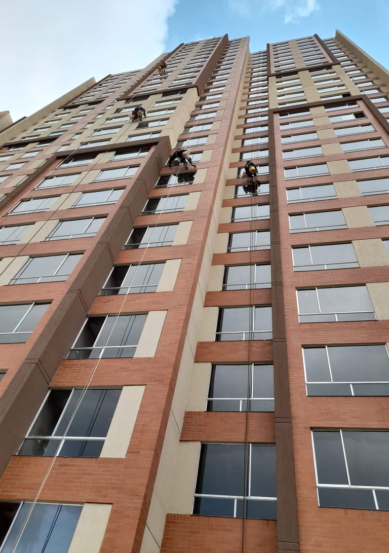 Professional window cleaners rappelling down a modern high-rise brick apartment building to wash exterior glass.