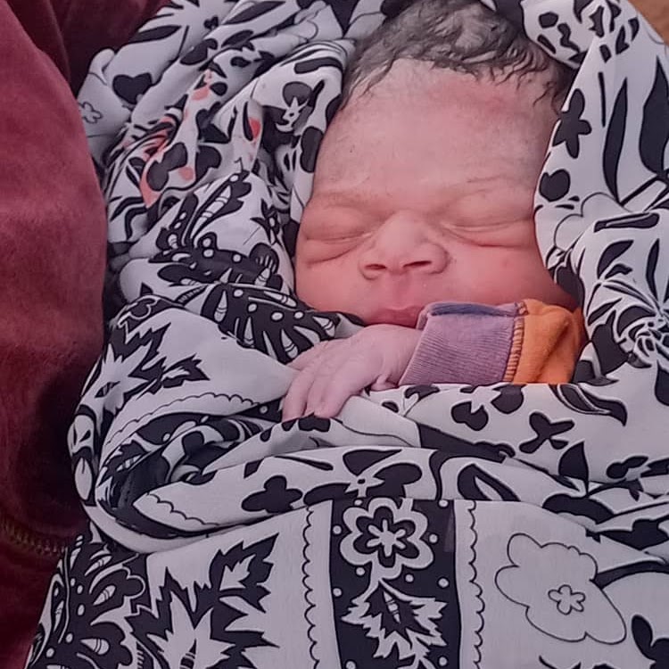 A sleeping newborn baby wrapped in a black and white patterned floral swaddle blanket.