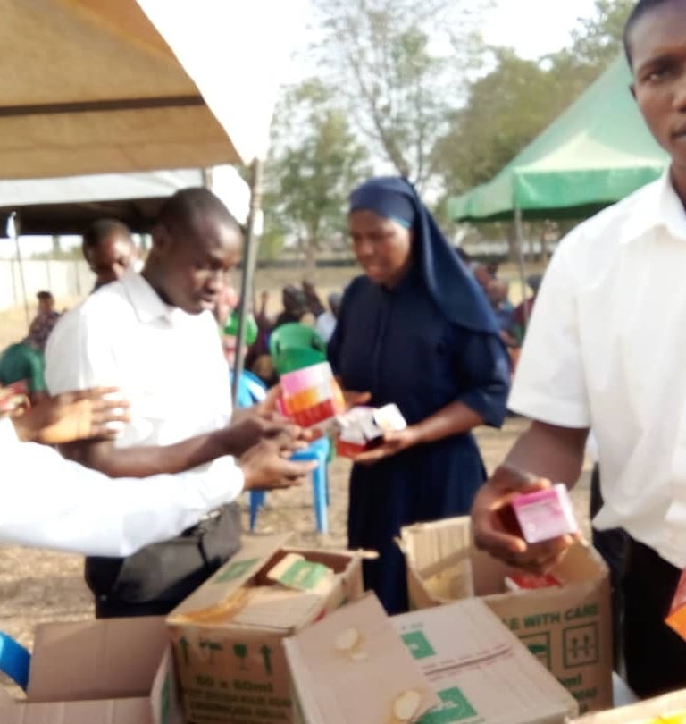 Health workers and a nun distributing essential medicine and supplies at an outdoor community outreach event.
