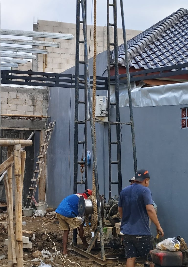 Construction workers operating a vertical deep well drilling machine for water access at a residential site.