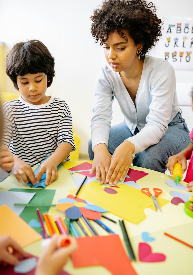 Uma terapeuta com cabelos cacheados orienta atentamente uma criança em uma atividade de dobradura de papel colorida