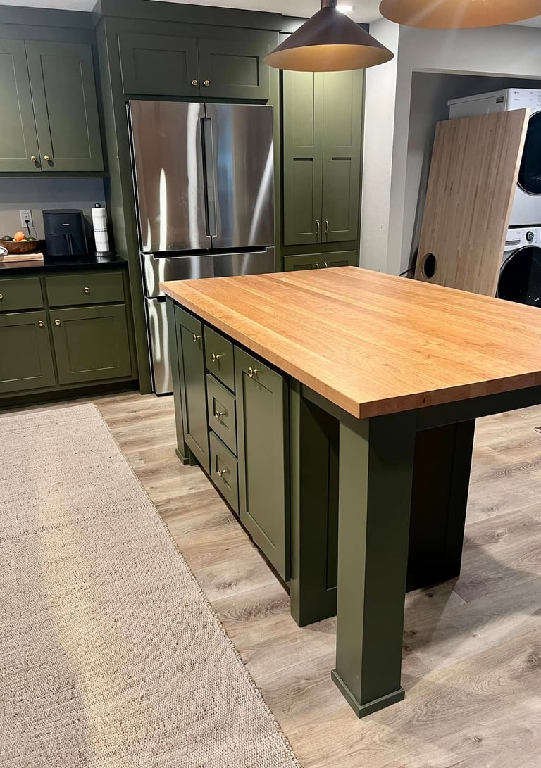 Modern green kitchen cabinets with a butcher block island and stainless steel refrigerator.