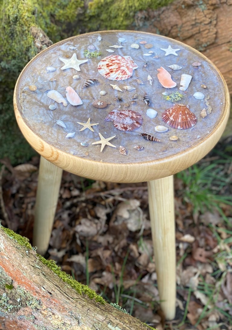 a small table with top inlay of shells atop the sand and set in resin