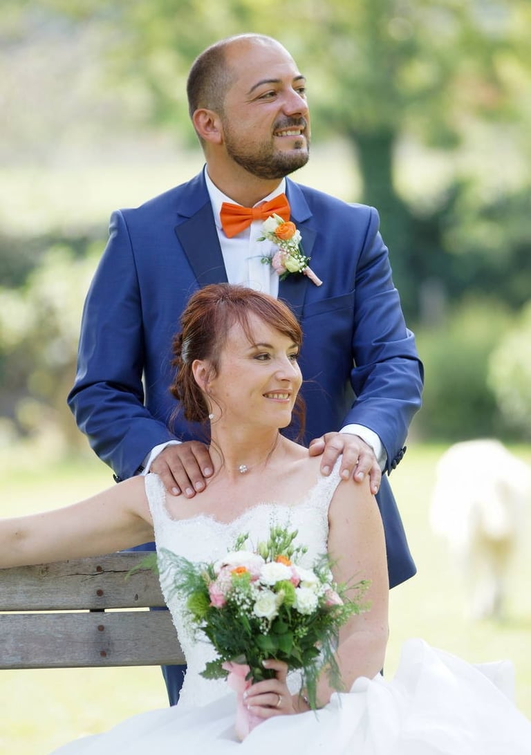 photo de couple pendant un mariage. la mariée est assise avec son bouquet comportant du orange