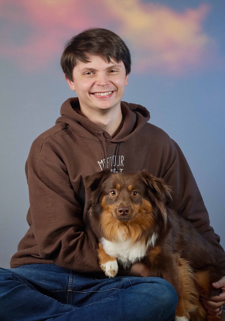 A smiling man in a brown hoodie sitting and holding his brown and white Australian Shepherd dog.