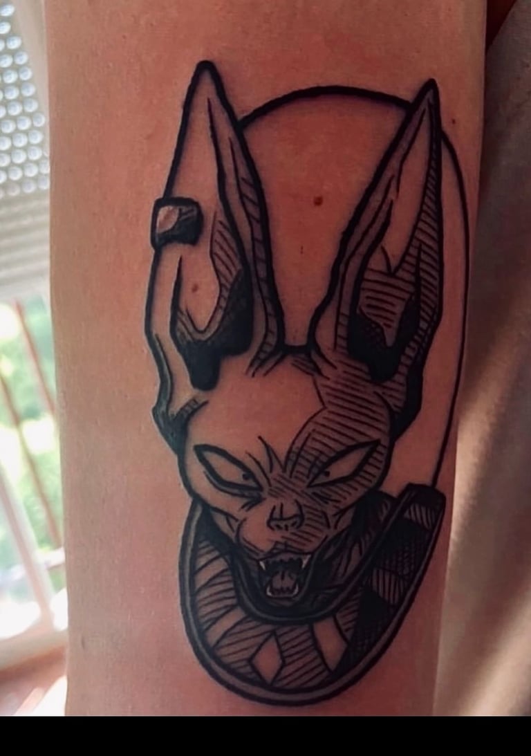 A detailed black and white tattoo of Beerus, the God of Destruction from Dragon Ball Super, with his signature smirk and