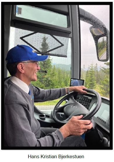 a smiing man in profile with a blue hat driving a bus