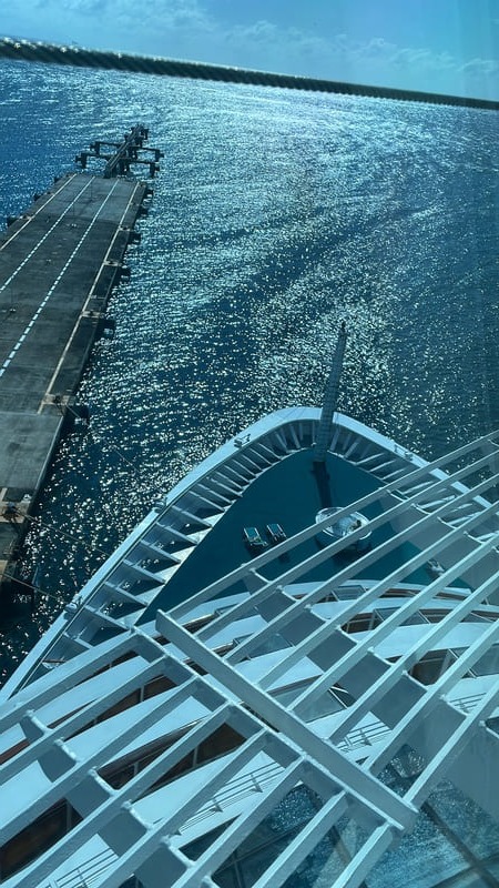 Luftaufnahme des Bugs eines Kreuzfahrtschiffs, das an einem tropischen Hafenpier über glitzerndem