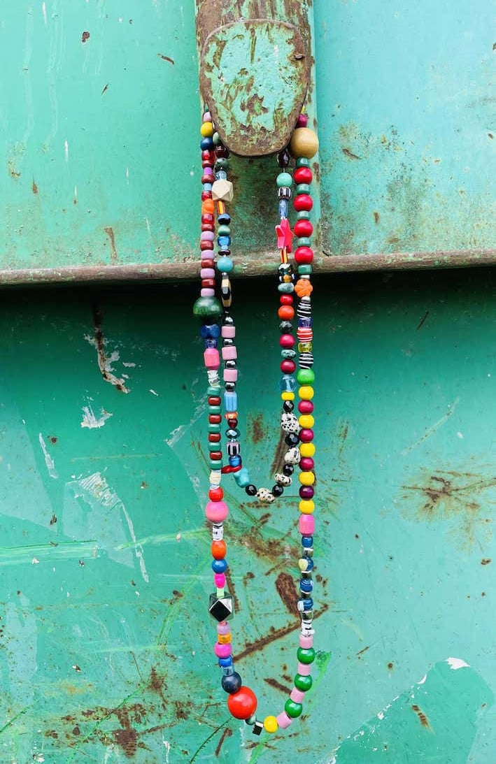 Handmade colorful beaded necklaces hanging on a rustic teal metal surface.