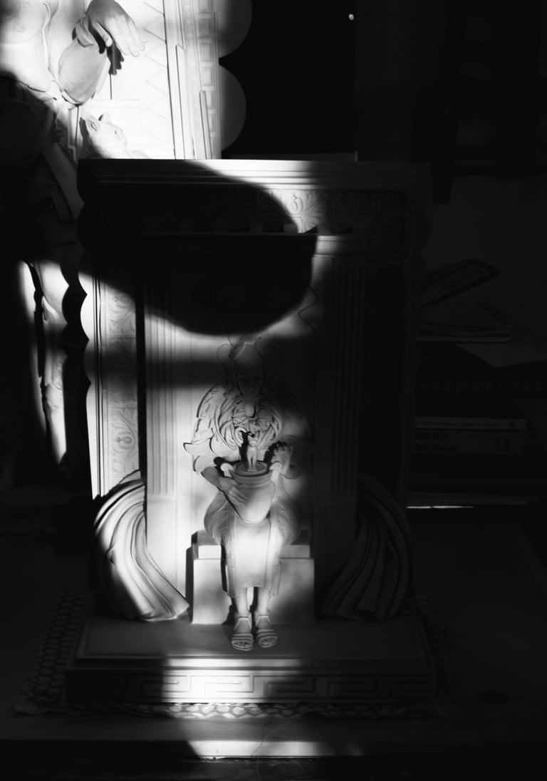 Shadow of the artist in her studio taking a photo of her sculpture half in sunlight, half in darkness.